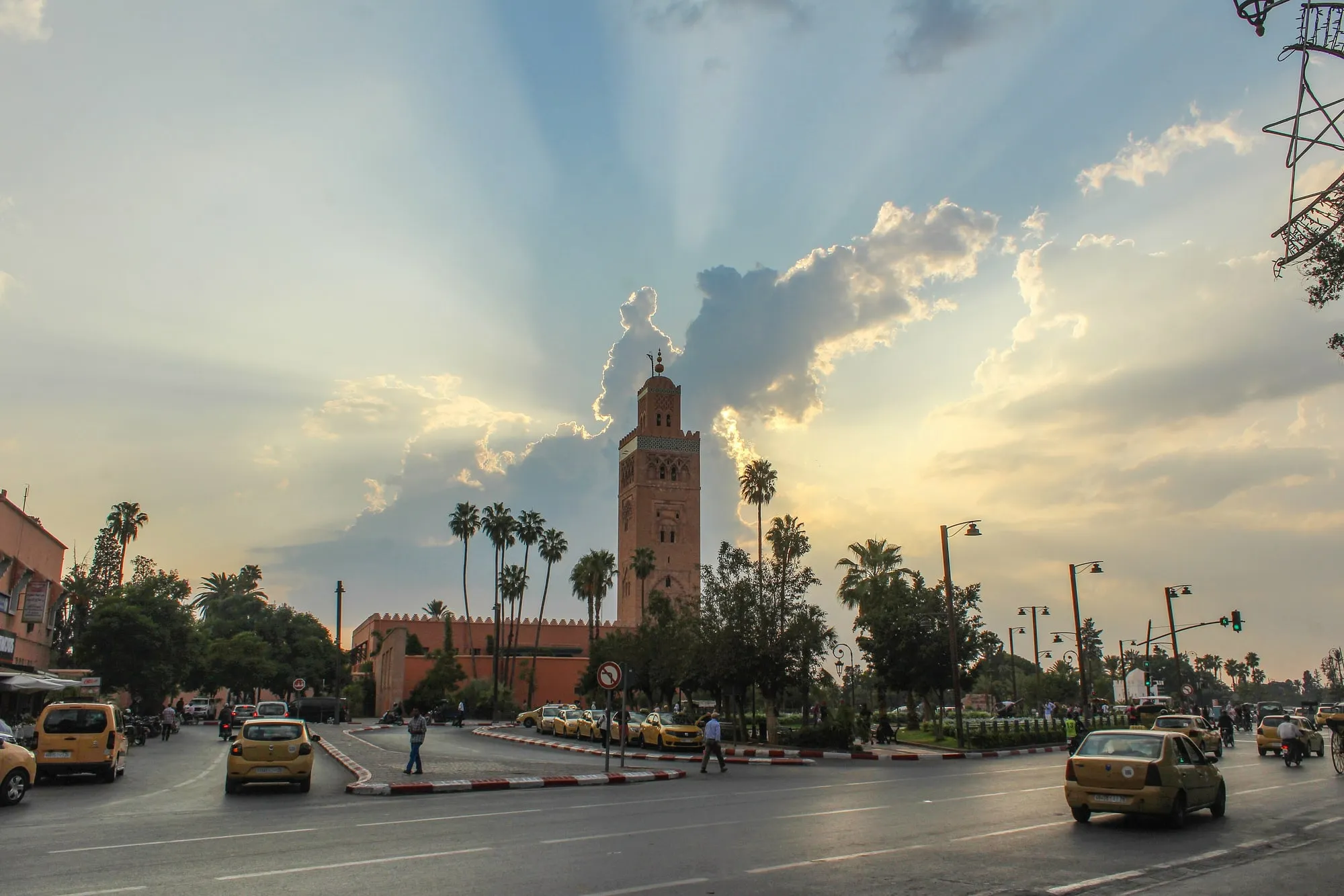 Le minaret de la Koutoubia au coucher du soleil, avec l'avenue animée et les palmiers de Marrakech